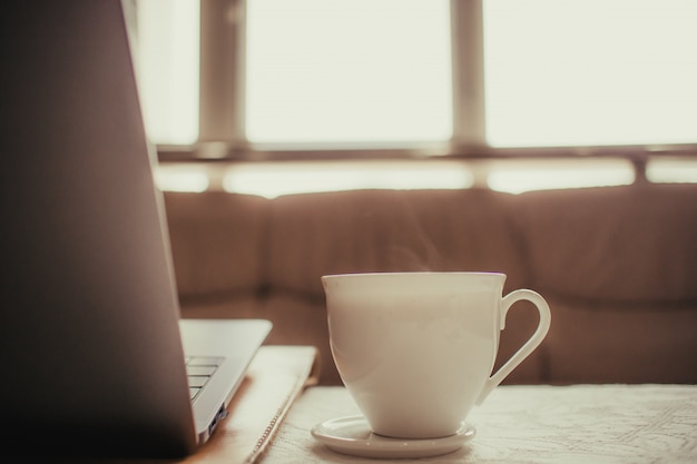 White cup of hot coffee on the table of a freelance man.