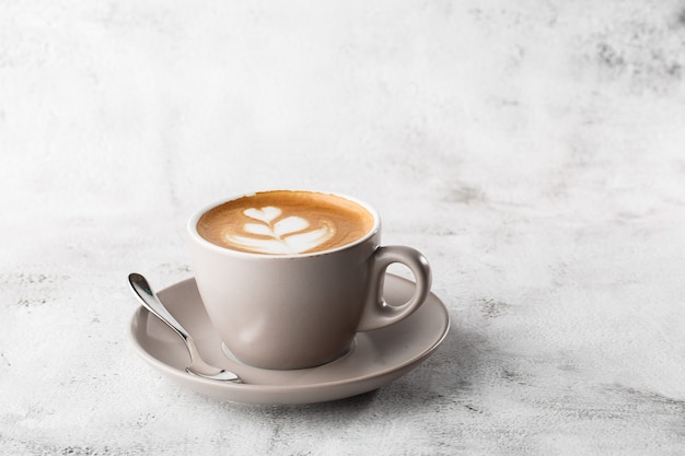 White cup of hot latte coffee with beautiful milk foam latte art texture isolated on bright marble background. Overhead view, copy space. Advertising for cafe menu. Coffee shop menu. Horizontal photo.