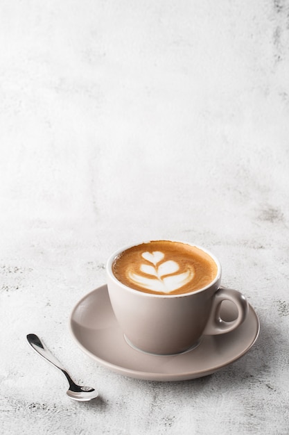 White cup of hot latte coffee with beautiful milk foam latte art texture isolated on bright marble background. Overhead view, copy space. Advertising for cafe menu. Coffee shop menu. Vertical photo.