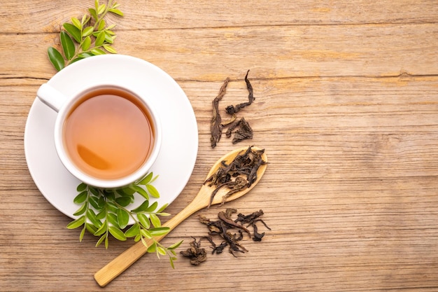 White cup of hot tea and dry tea leaf on wooden table