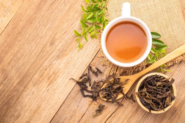 White cup of hot tea and dry tea leaf on wooden table