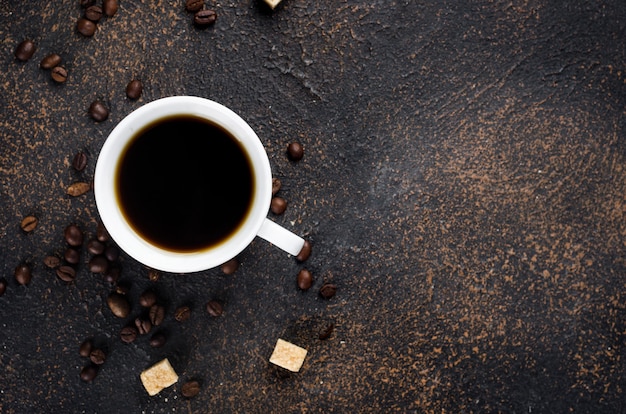 Photo white cup of i black coffee and coffee beans on dark concrete background. the concept of hot drinks, invigorating breakfast.