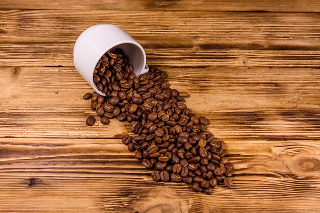 White cup and scattered coffee beans on rustic wooden table