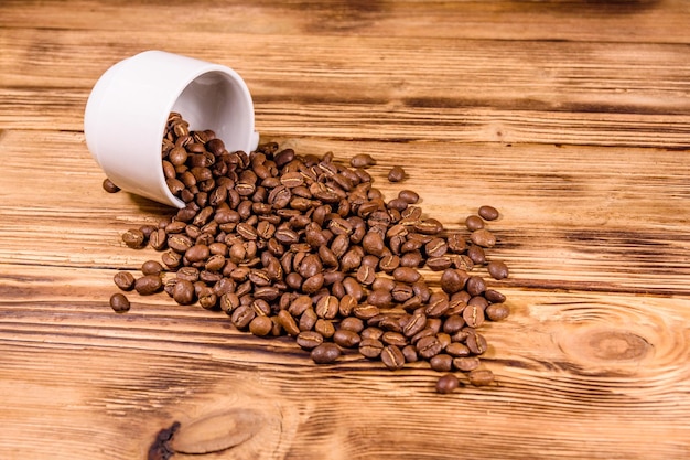 White cup and scattered coffee beans on rustic wooden table