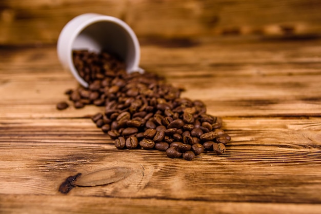 White cup and scattered coffee beans on wooden table