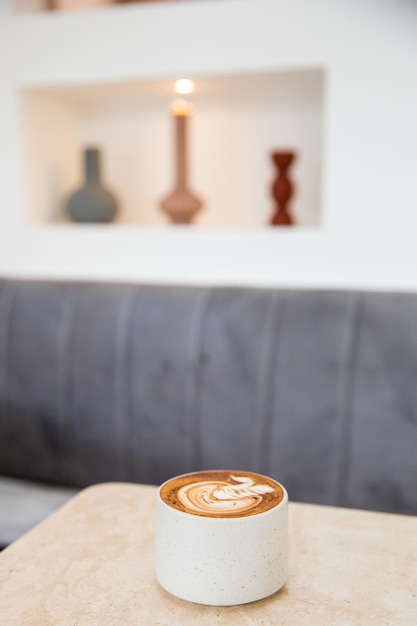 White cup of tasty cappuccino with latte art on white marble background in cafe