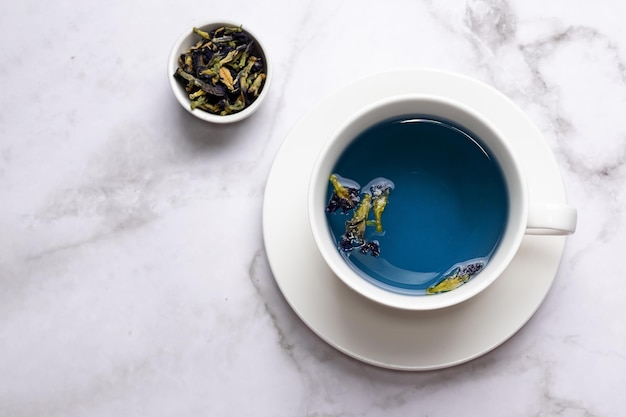 White cup with anchan from butterfly pea flower on marble background, healthy herbal blue tea.