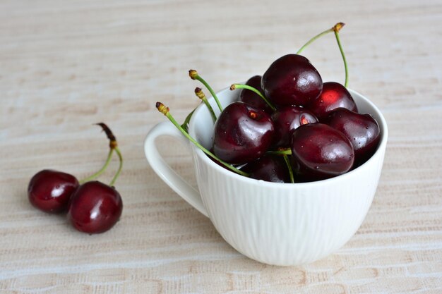 A white cup with dark cherries on a table isolated