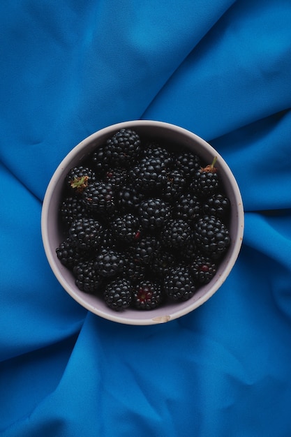 Photo white cup with fresh blackberries on a blue cloth