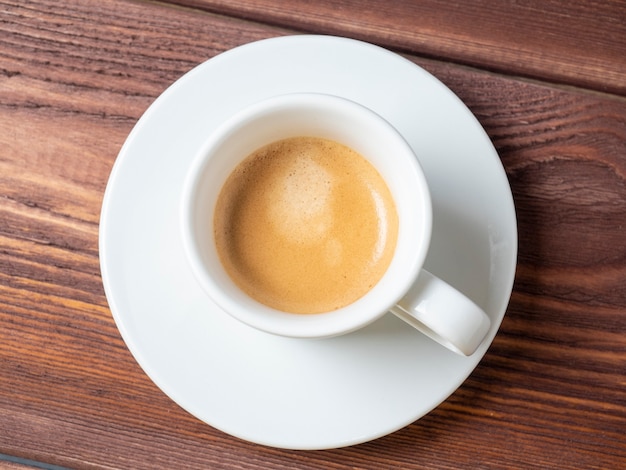 White cup with freshly brewed espresso on a wooden background. Top view, flat lay, brown foam. Coffee concept