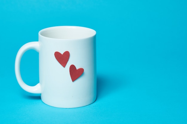 White cup with red hearts isolated on a blue background