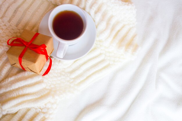 White cup with tea on a light and a box with a gift.