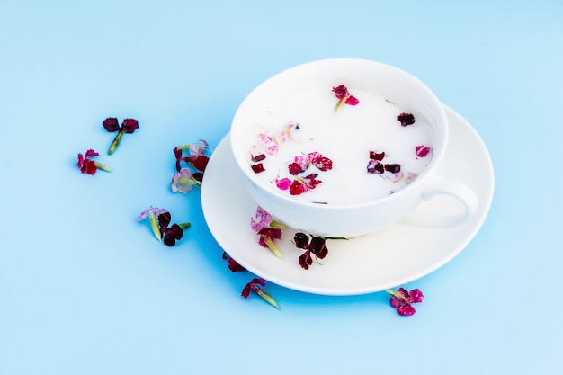 White Cup with vegan milk and flowers on a blue background. Concept of vegetarian drinks and food, herbal teas, beauty and health, Spa.