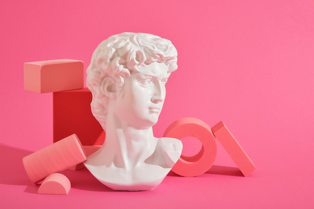 White decorative sculptural bust and several pink geometric coasters on a pink background