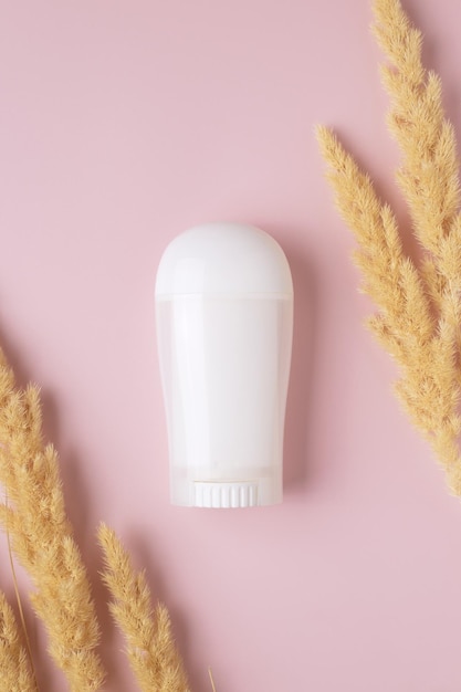 White deodorant and dry pampas grass on pink background