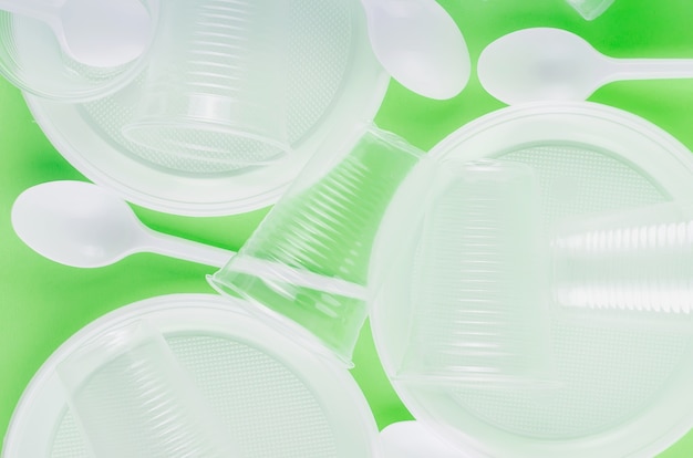 White Disposable cups, plates, forks, knives on light green background closeup