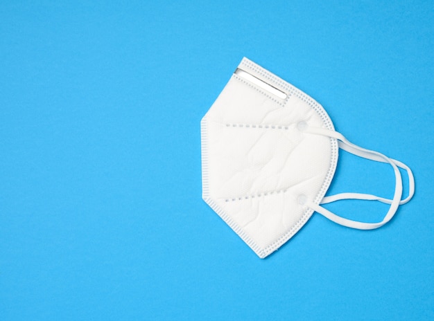 White disposable medical mask on a blue background, personal protective equipment for the respiratory tract from viral infections, top view