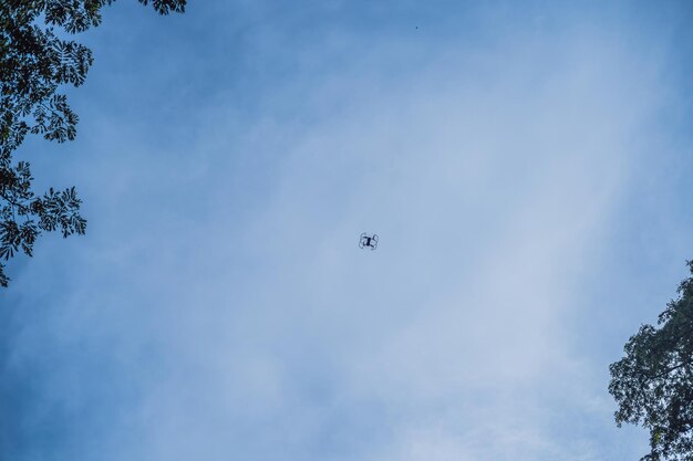 White drone flying against the sky and trees