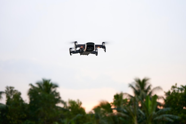 White drone flying over jungle forest against sunset sky