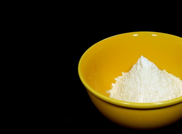 White dry flour in yellow ceramic bowl on black background 