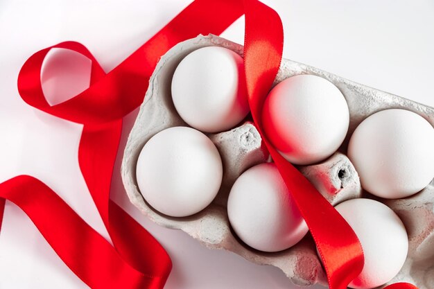 White easter eggs in ecofriendly cardboard box with red festive silk ribbon on white background