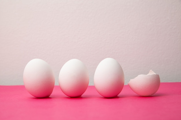 White eggs near broken shell on pink table