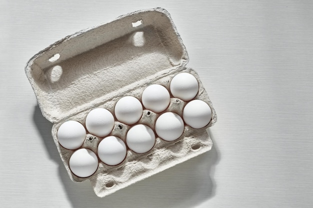 White eggs in paper egg box Chicken eggs Cardboard egg box on the white table in sun ling with shadow Top view