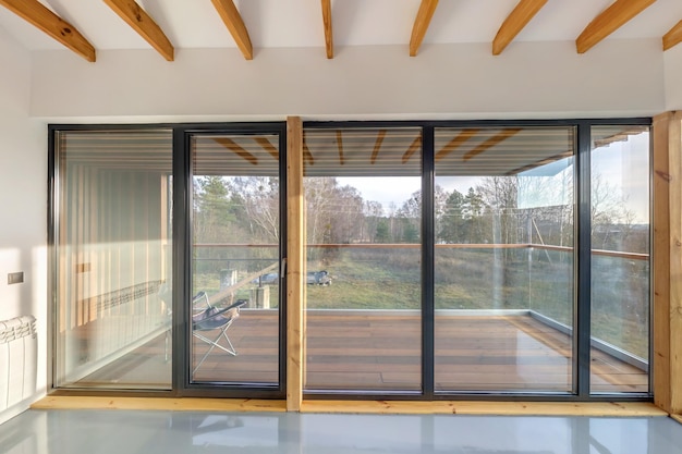 White empty apartment interior with panoramic windows and wooden rafter ceiling in vacation homestead house Overlooking the nature in forest