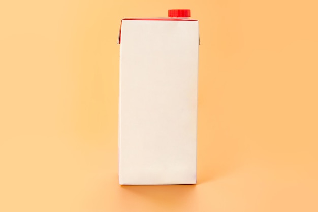 A white empty blank paper package of milk with a red cap stands on orange background Nutrition Copy space Mockup Mockup Paper Design Empty