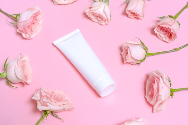 White empty cosmetic tube on a pink background with delicate pink roses