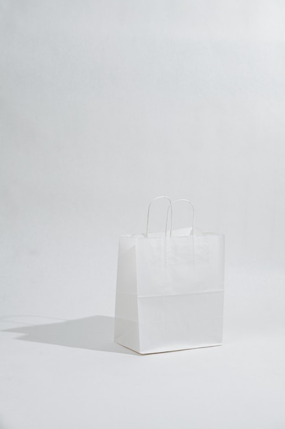 White empty paper bag with rope handles casting a shadow over white background