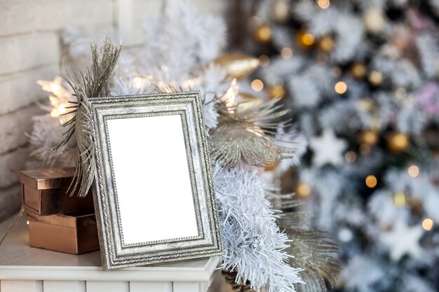 White empty photo frame on the fireplace. Christmas white interior with bokeh defocused effect