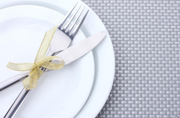 White empty plates with fork and knife tied with a ribbon on a grey tablecloth