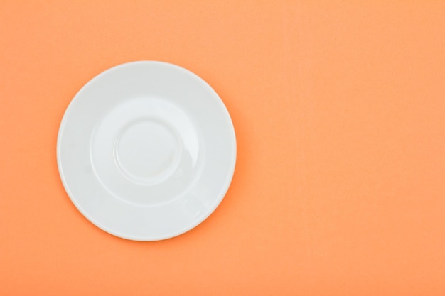 White empty porcelain saucer on peach color background with copy space Top view with copy space