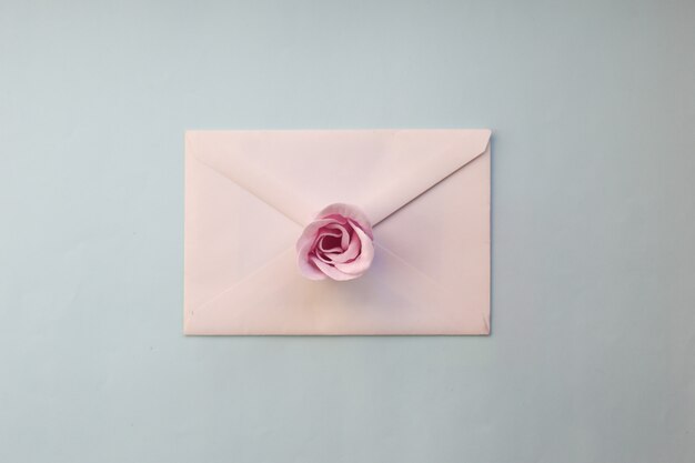 White envelope with pink rose flower on a blue background