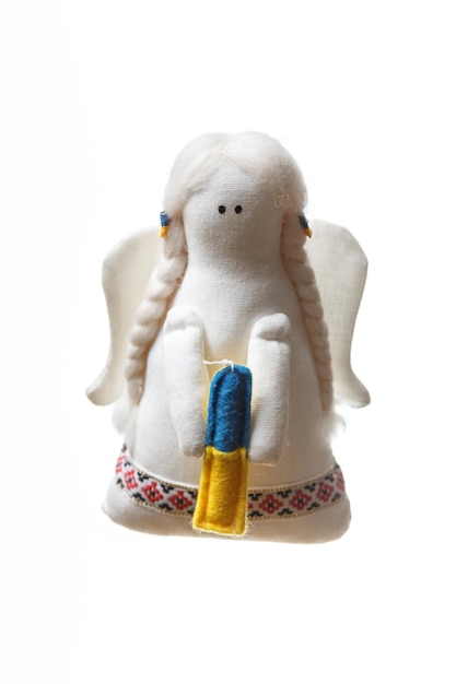 White fabric soft angel toy with wings holding a candle with a color of ukrainian flag blue and yellow