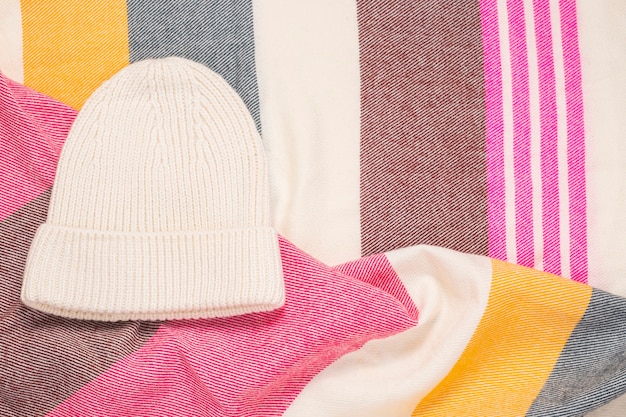 White female hat on a striped scarf. Top view, flat lay.