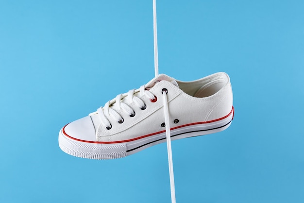 White female sport sneakers with shoe lace against blue background casual trendy shoes closeup creat