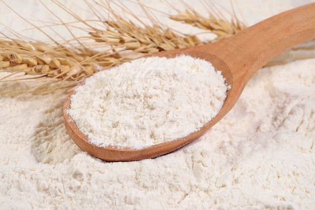 White flour in a wooden spoon and ears of wheat on a white flour