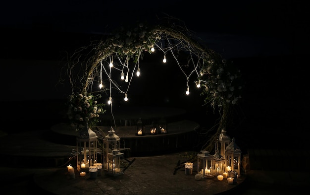 White flowers arch at the wedding ceremony Outdoors decoration Romantic rustic style Lamps lights in the evening