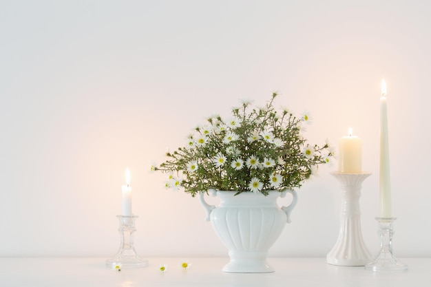 White flowers in white ceramic vase with burning candles in white interior