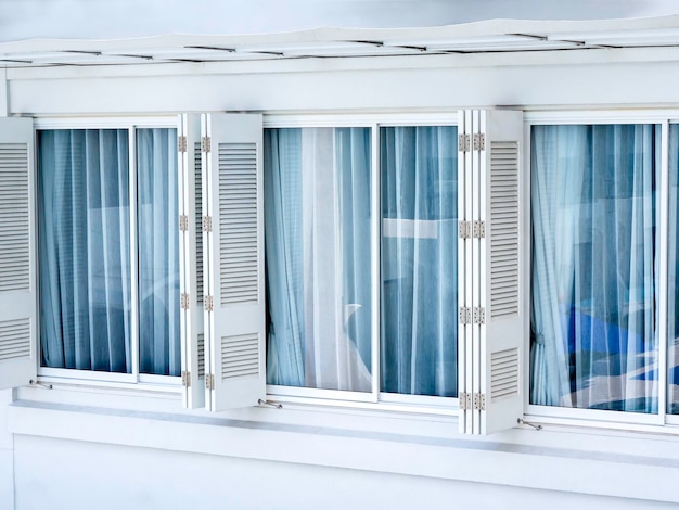 White folding wooden shutter with glass windows and blue curtains on white building Asian style window exterior design