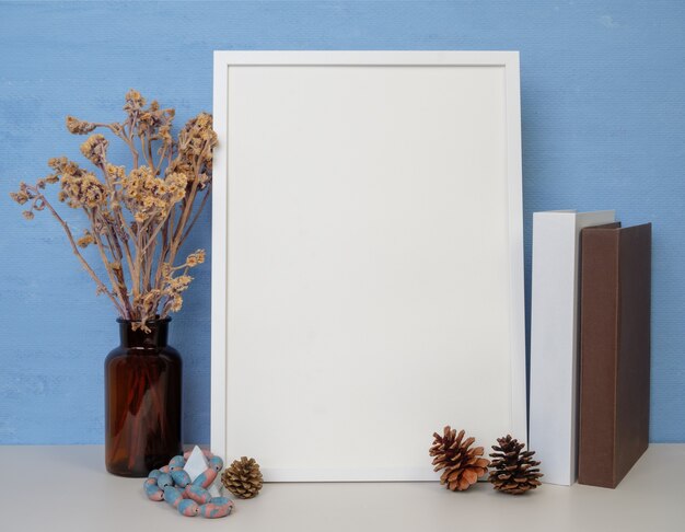 White frame mockup for design or text, books,dried flower in glass jar,pine cones and antique stone sitting on a wooden table blue wall background