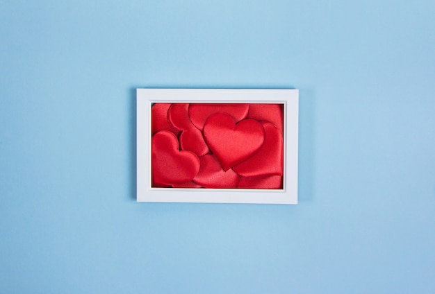 White frame with red hearts on blue background, copy space, valentine's day, love, invitation