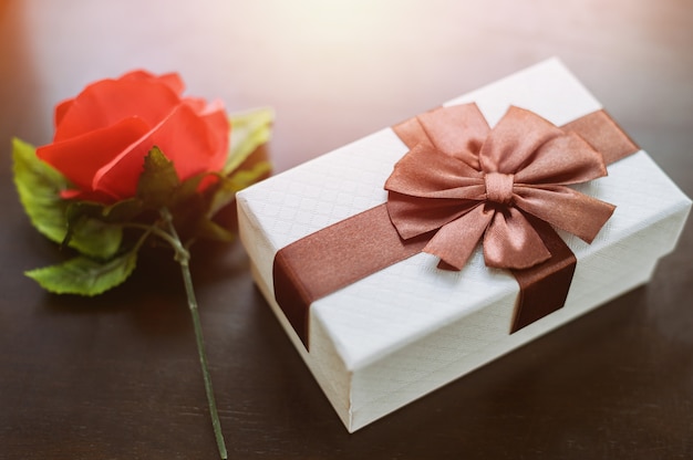 White gift box and red rose on wooden table