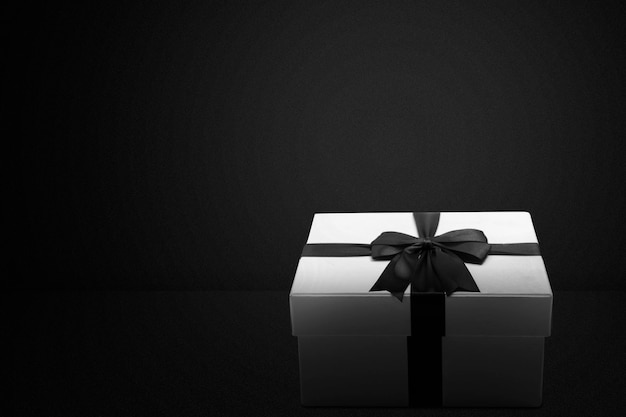 White gift box with a black ribbon with a black background. Black Friday concept