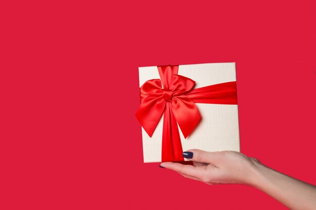 White gift box with a red bow in his hand on red 