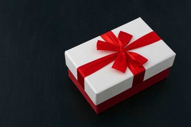 White gift box with red ribbon and bow on black background.