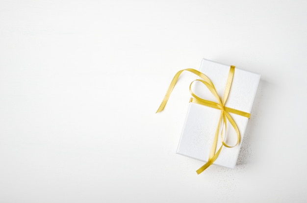 White gift box with sparkles and golden ribbon on white