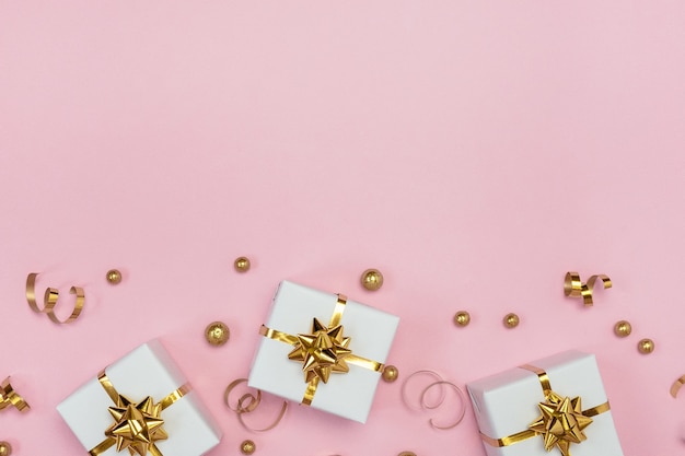 White gift boxes, golden decorations and ornaments on pastel pink background. Flat lay, copy space.